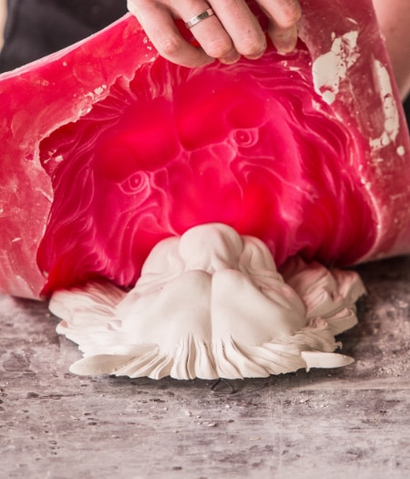 A man peels a red silicone mould from a cast of a lion's head